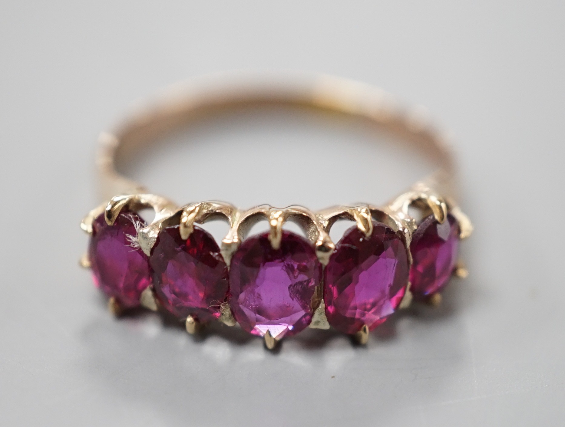 An early 20th century yellow metal and graduated five stone ruby set half hoop ring, size O, gross weight 2.6 grams.